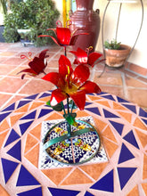 Load image into Gallery viewer, Red metal lily garden decor sculpture placed on a patterned mosaic table in an outdoor patio setting.