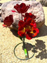 Load image into Gallery viewer, Metal red garden roses in a green wire stand, placed outdoors in front of a large rock.