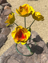 Load image into Gallery viewer, Yellow metal rose garden sculpture with four roses, mounted on a green wire stand and photographed outdoors on a rock with sand and rocks in the background.
