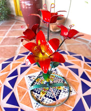 Load image into Gallery viewer, A decorative metal flower arrangement with red lily blooms and green stems, displayed on a patterned ceramic tile table in a patio setting.
